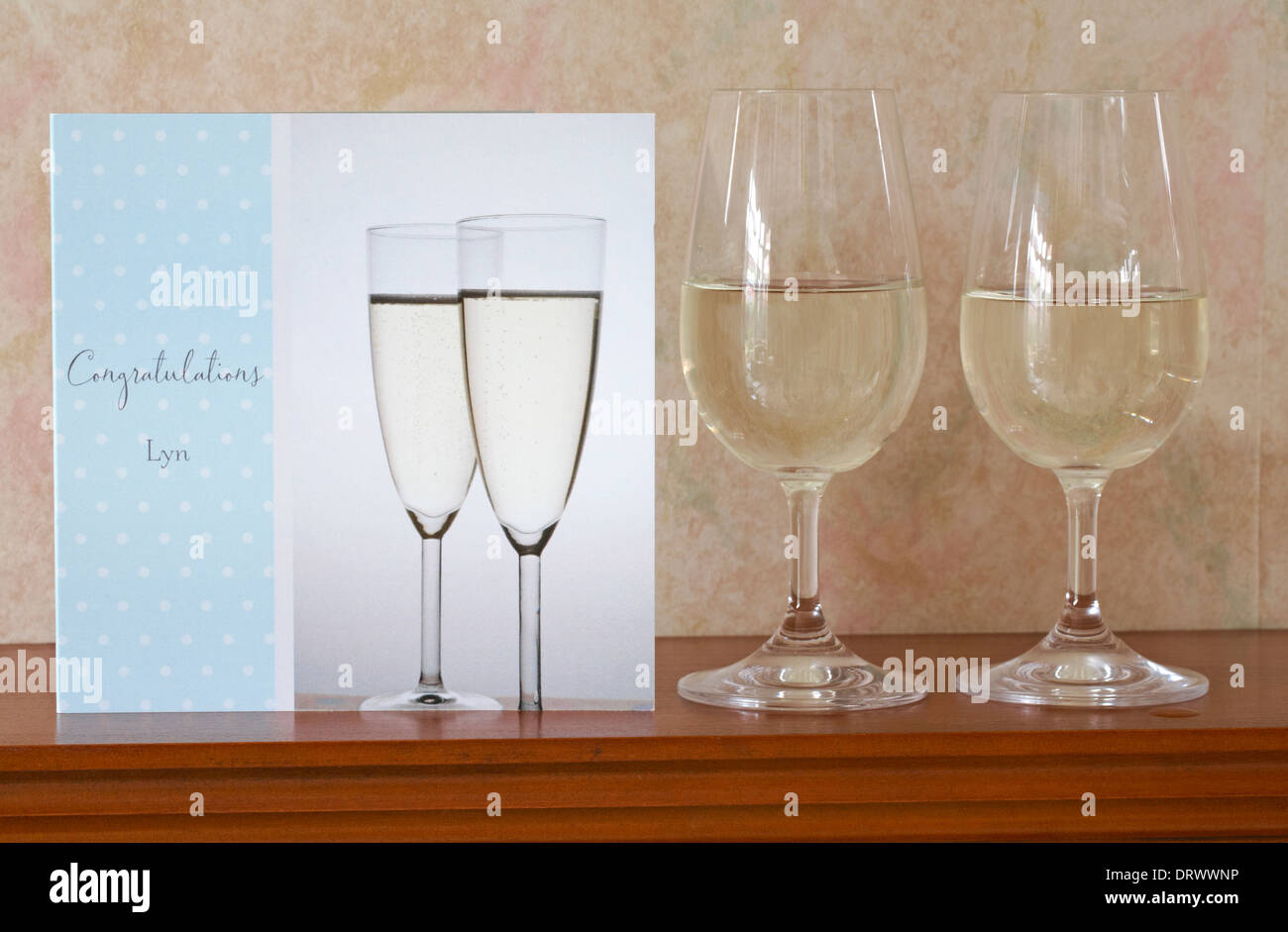 Glückwunschkarte mit zwei Gläsern Wein auf Mantelstück in der Lounge - Celebration Celebrate Concept Stockfoto