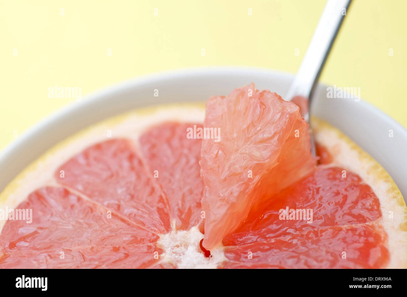 Halbe rosa Grapefruit zugeschnitten, mit einem Abschnitt wird herausgenommen, mit einem Löffel zu essen. Stockfoto