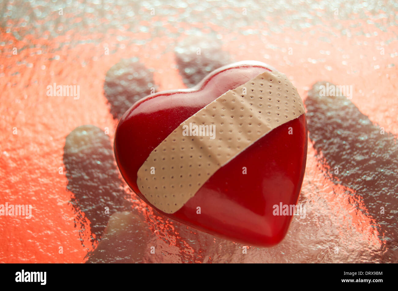 Herz mit Heftpflaster unter Glas mit der hand gehalten. Stockfoto