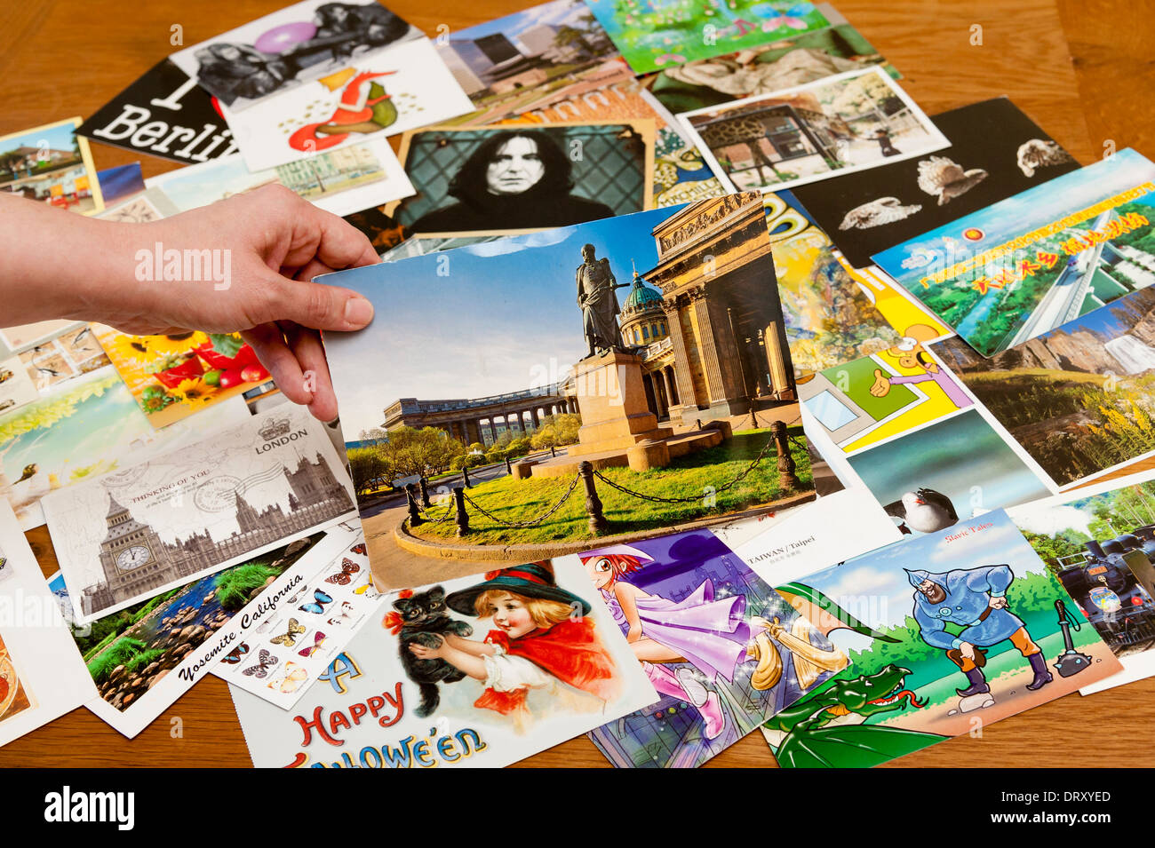 Eine Vielzahl von Postkarten liegt auf einem Tisch, mit einer Hand hält man aus Russland im Vordergrund. Stockfoto