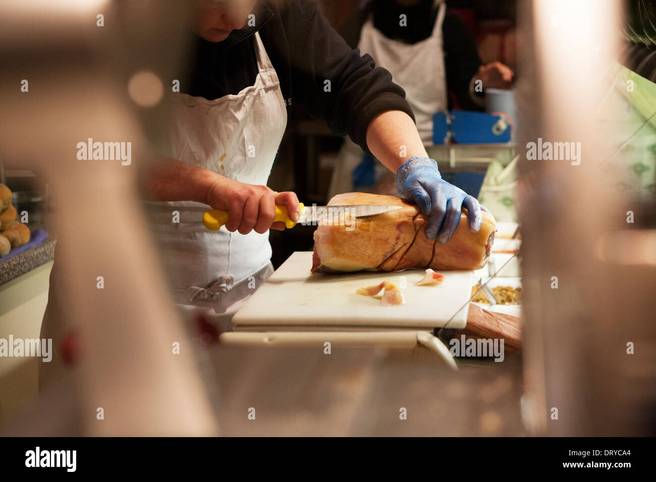 Eine weibliche Metzger schneiden einen Schinken (Schweinefleisch) gemeinsame. Stockfoto