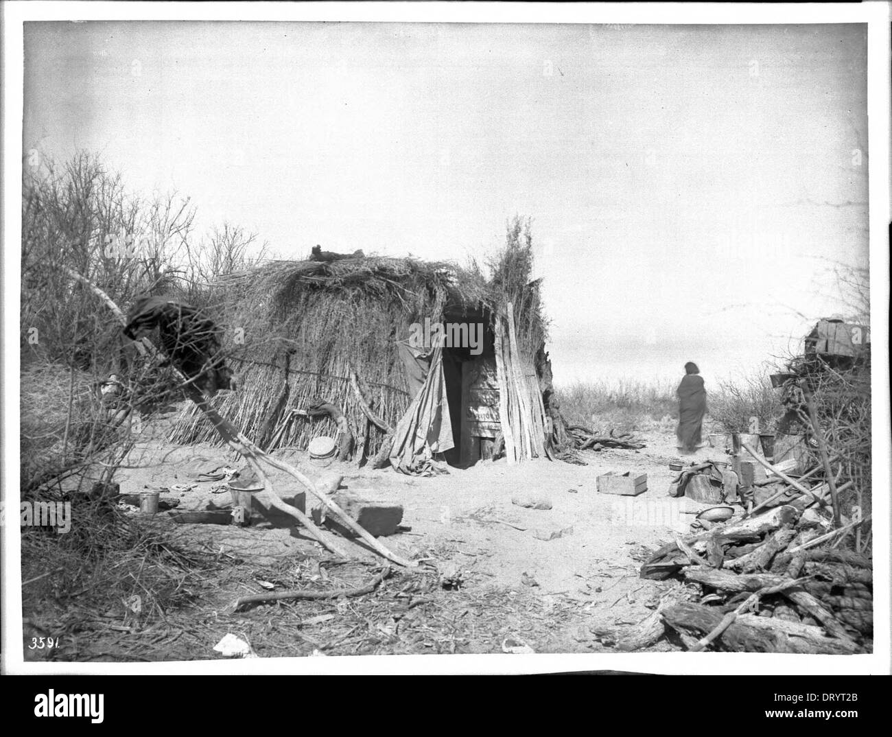 Ein Apachen-Indianer steht in der Nähe eines Kan- oder Bürstenhauses auf der Palomas-Indianerreservation um 1900. Stockfoto
