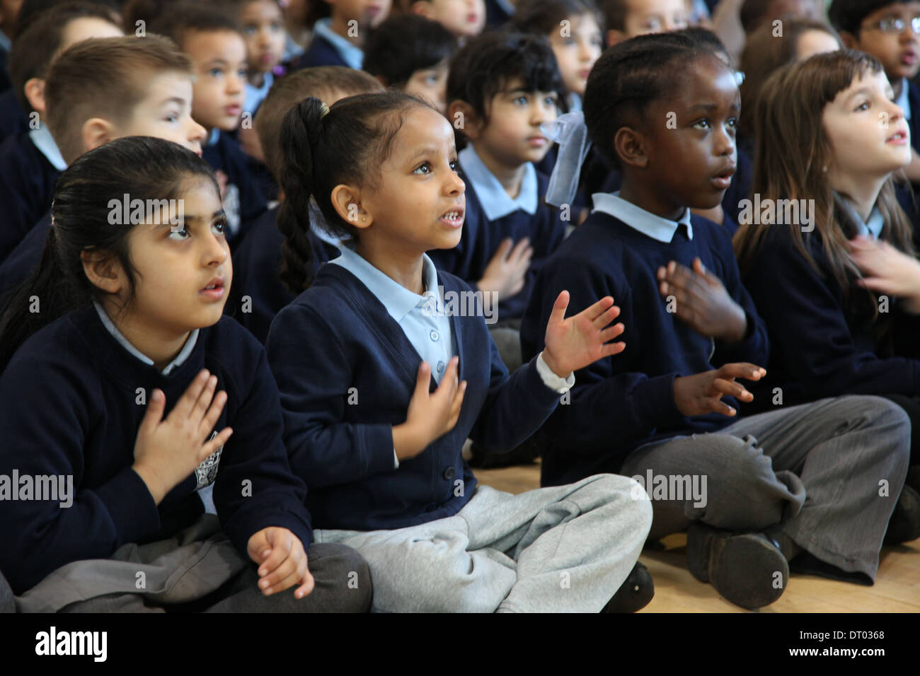 Kinder bei einer Schulversammlung singen, Händeklatschen und Aktionen Stockfoto