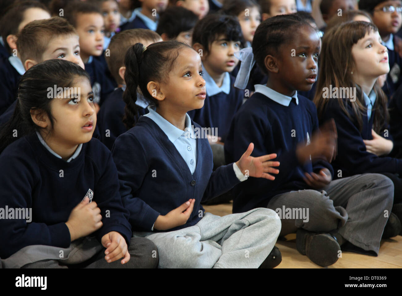 Kinder bei einer Schulversammlung singen, Händeklatschen und Aktionen Stockfoto