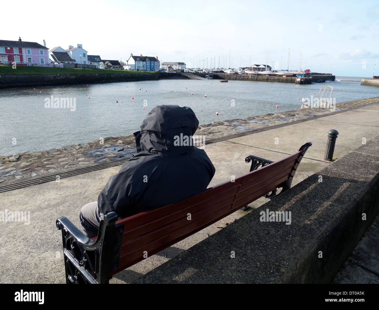 Mann im Anorak sitzen auf einer Bank am Hafen von Aberaeron Ceredigion Wales UKKATHY DEWITT Stockfoto