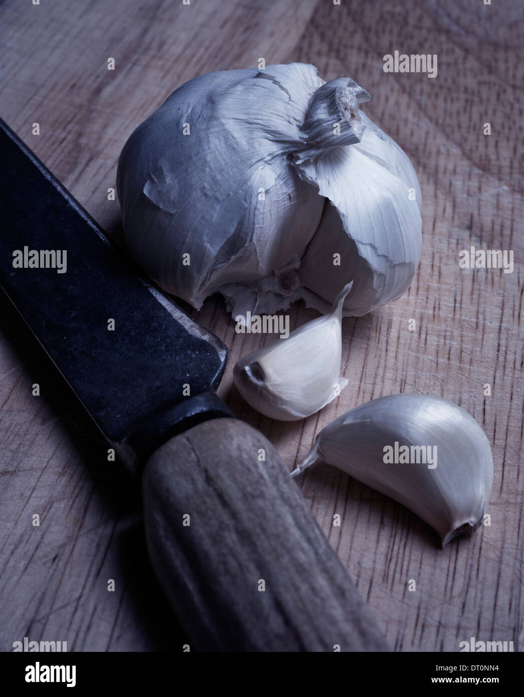 Knoblauchzehe sitzt separat vor Knoblauchzwiebel auf rustikalen Holztisch. Rustikal, Knochen behandelt Messer begleitet Knoblauch. Stockfoto