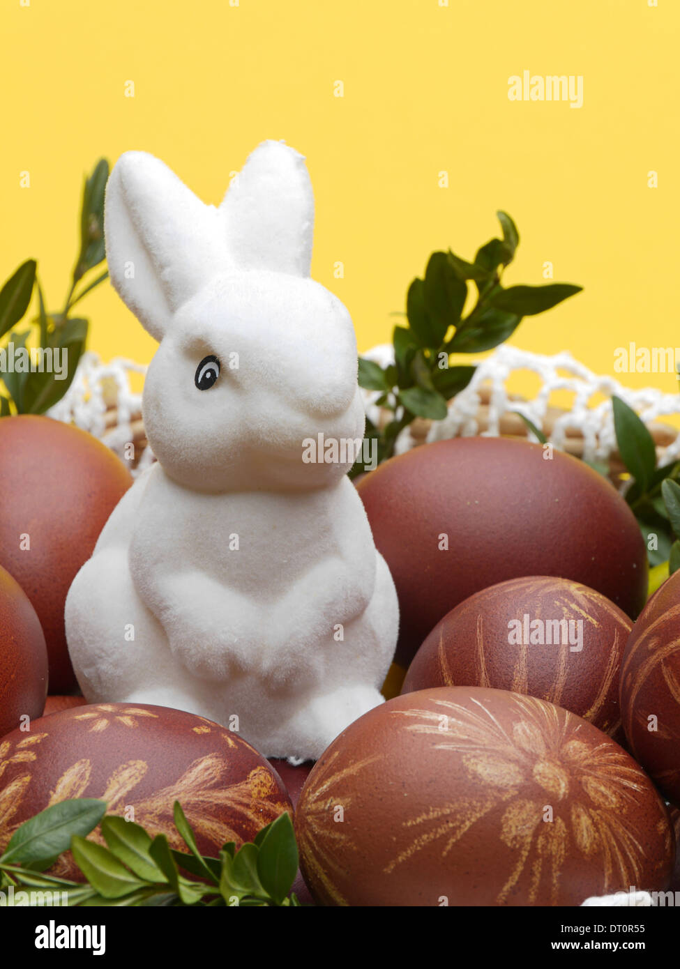 Weiße Plüsch Osterhase im Korb voller Ostern Eiern auf gelbem Hintergrund Stockfoto