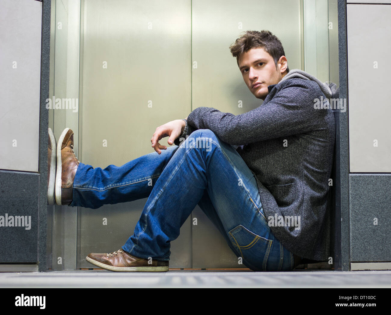 Hübscher junger Mann sitzt vor Aufzugtüren, Blick in die Kamera Stockfoto