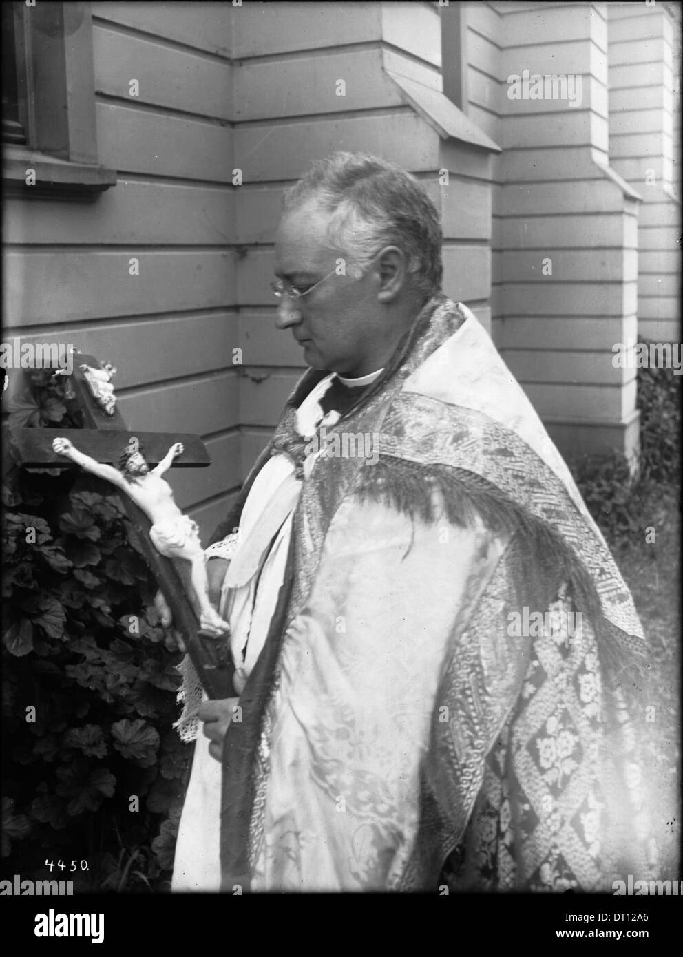 Dieses Foto zeigt Pater Reposo, der 1908 ein Kruzifix in der Mission San Jose hält und einen Moment religiöser Hingabe und die historische Bedeutung der Mission festnimmt. Stockfoto