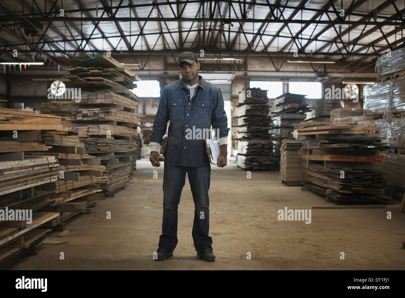 Ein Haufen von recycelten aufgearbeiteten Holzbohlen von Holz Reklamation in einem Holz Hof einen Mann im Werk Overall mit einem Klemmbrett Stockfoto