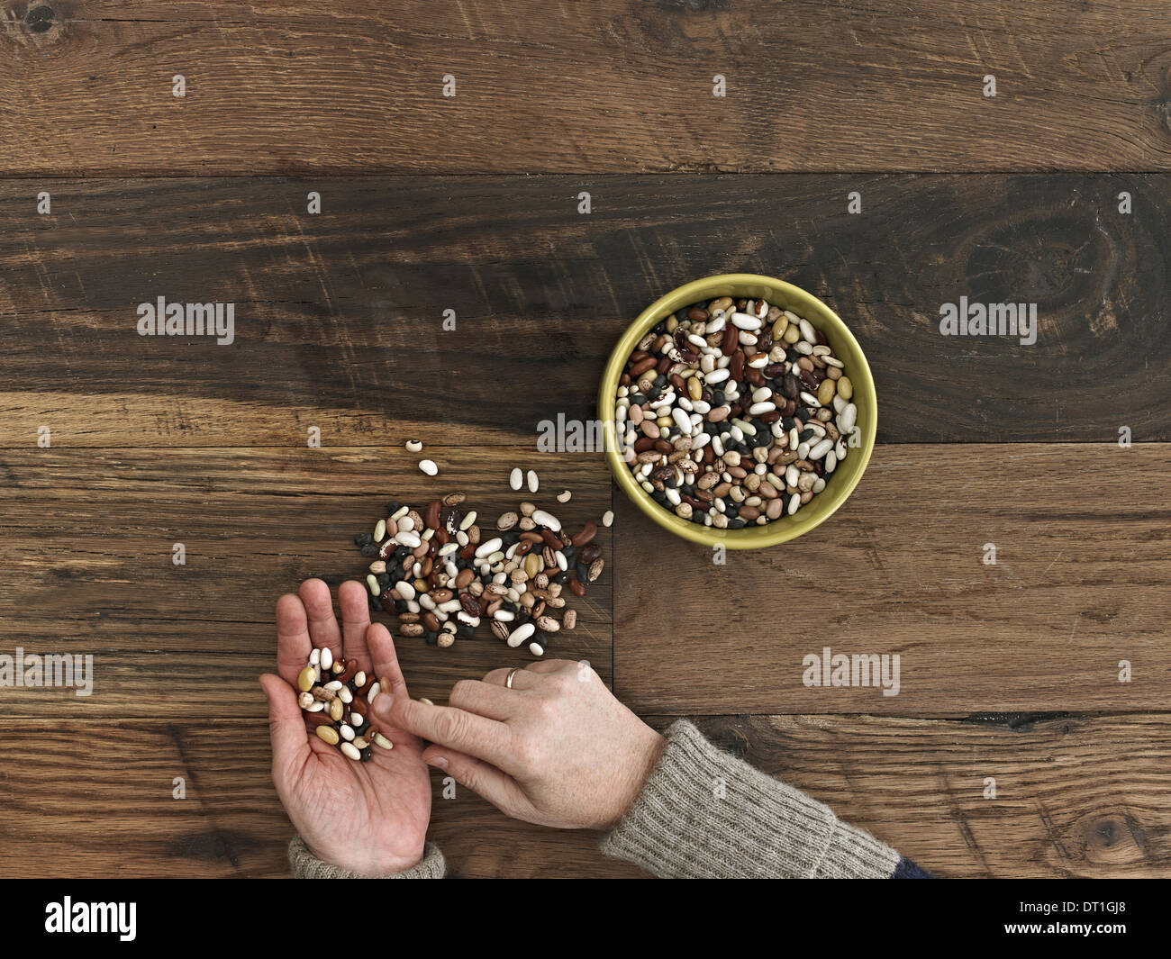 Eine Person, die verschiedene Arten von Bohnen und Hülsenfrüchte in ihren Händen auf einer hölzernen Tischplatte sortieren Stockfoto