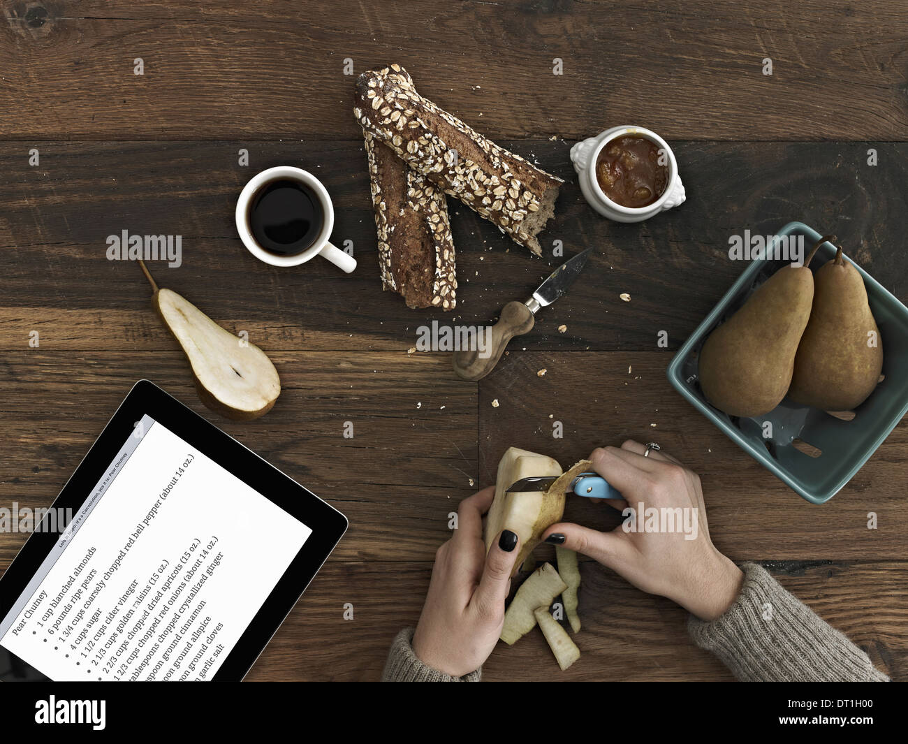 Eine Person mit einem Peeling Messer schälen einen Birne A Computer Tablet-Gerät mit dem Bildschirm Anweisungen ein Rezept Stockfoto