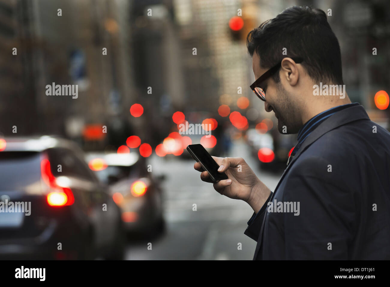 Ein Mann in eine dunkle Jacke Überprüfung sein Handy Stand auf einer belebten Straße in der Abenddämmerung Stockfoto