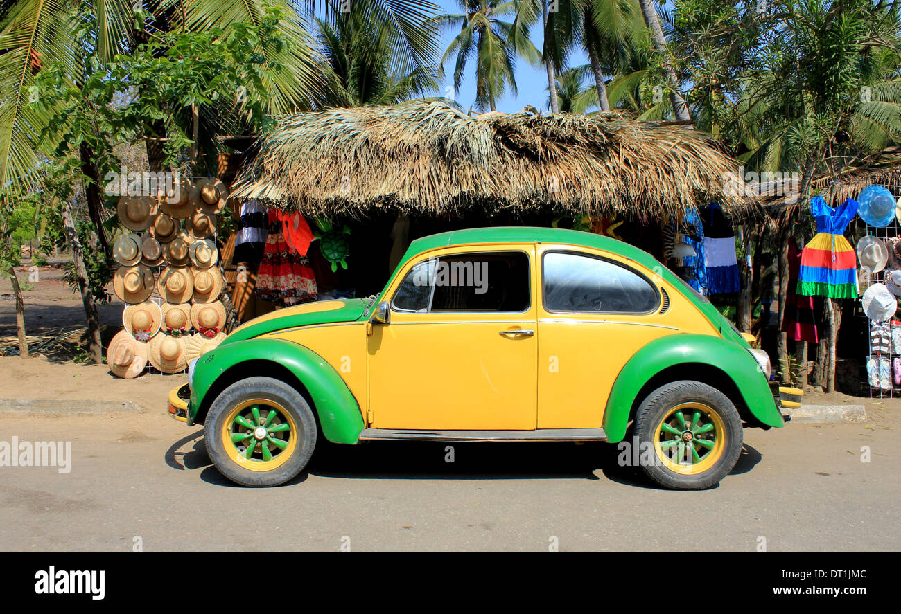 Gelb und grün VW Käfer Bug in der Nähe von Strand, Ventanilla, Oaxaca, Mexiko mit Palmendach Markt stehen hinter dem Verkauf von Hüten und Kleidung Stockfoto