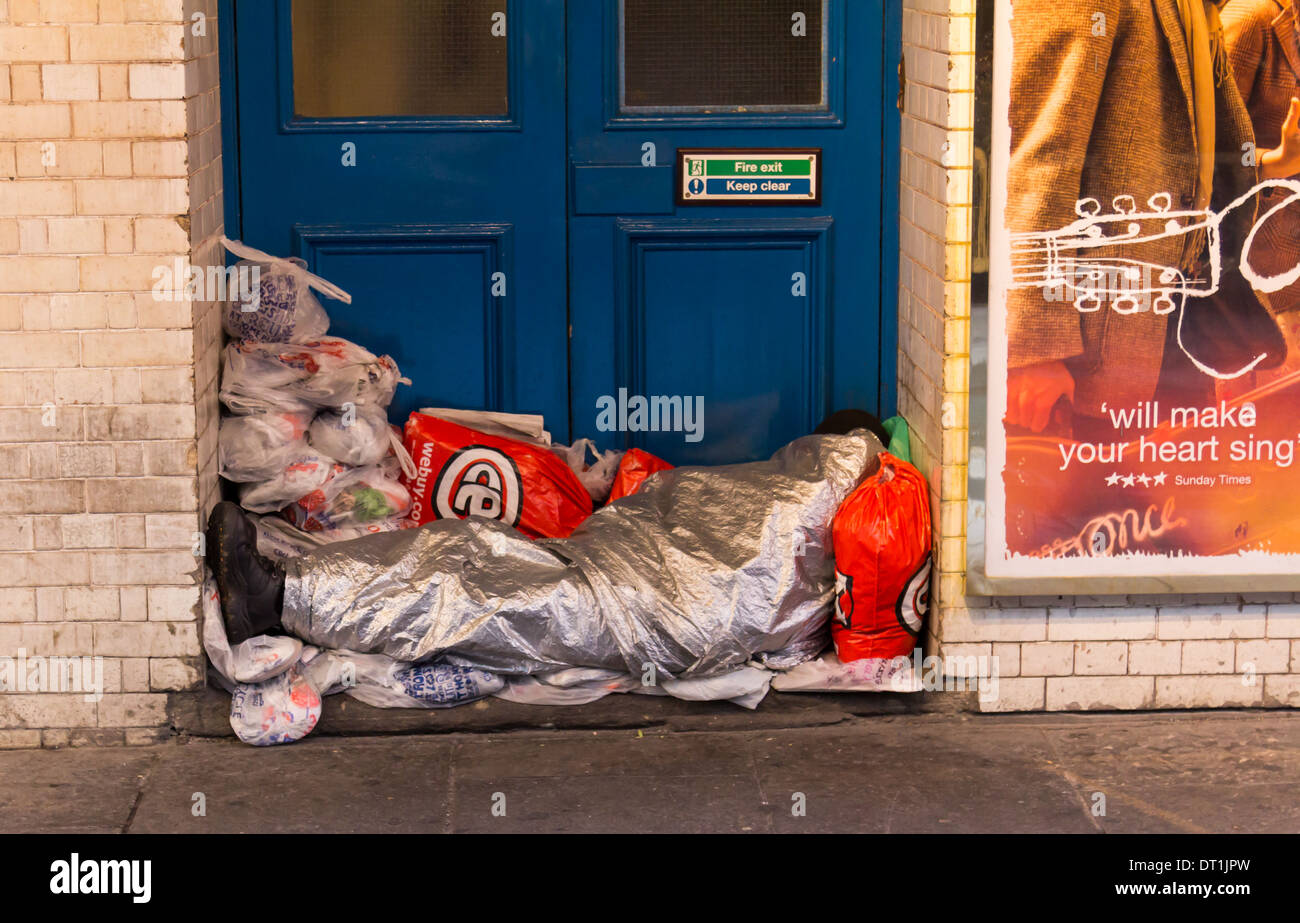 LONDON, UK 1. Februar 2014: ein Obdachloser eingewickelt in eine Decke Folie in einer Tür eines Gebäudes mit Plastiktüten alle Aroun Stockfoto