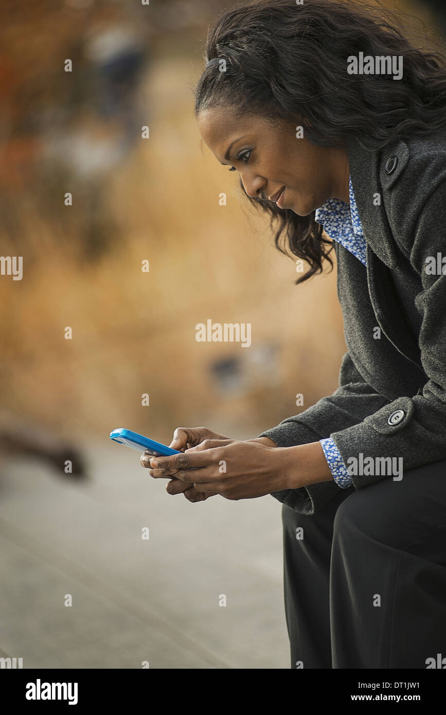 Eine Frau in einem Mantel zu überprüfen und SMS in Kontakt mit dem Handy telefonieren Stockfoto