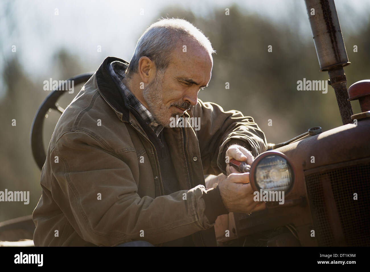 Arbeiten auf einem Bio Bauernhof-Mann in eine braune Jacke arbeiten an Landmaschinen Traktor Stockfoto