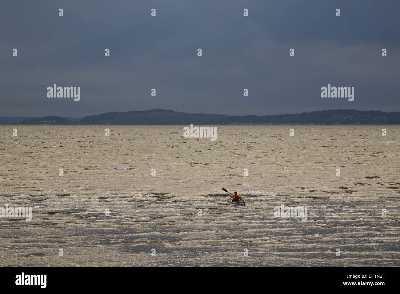 Ein Kajakfahrer Paddel seine Seekajak in den Puget Sound auf einen dunklen und trüben Abend Stockfoto