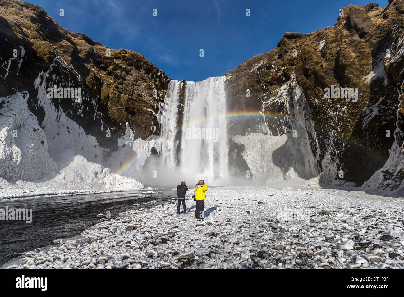 Regenbogen über Skogafoss Wasserfall im Winter Island Paar genießt die Nähe zu den Wasserfall mit einem schönen Regenbogen. Stockfoto