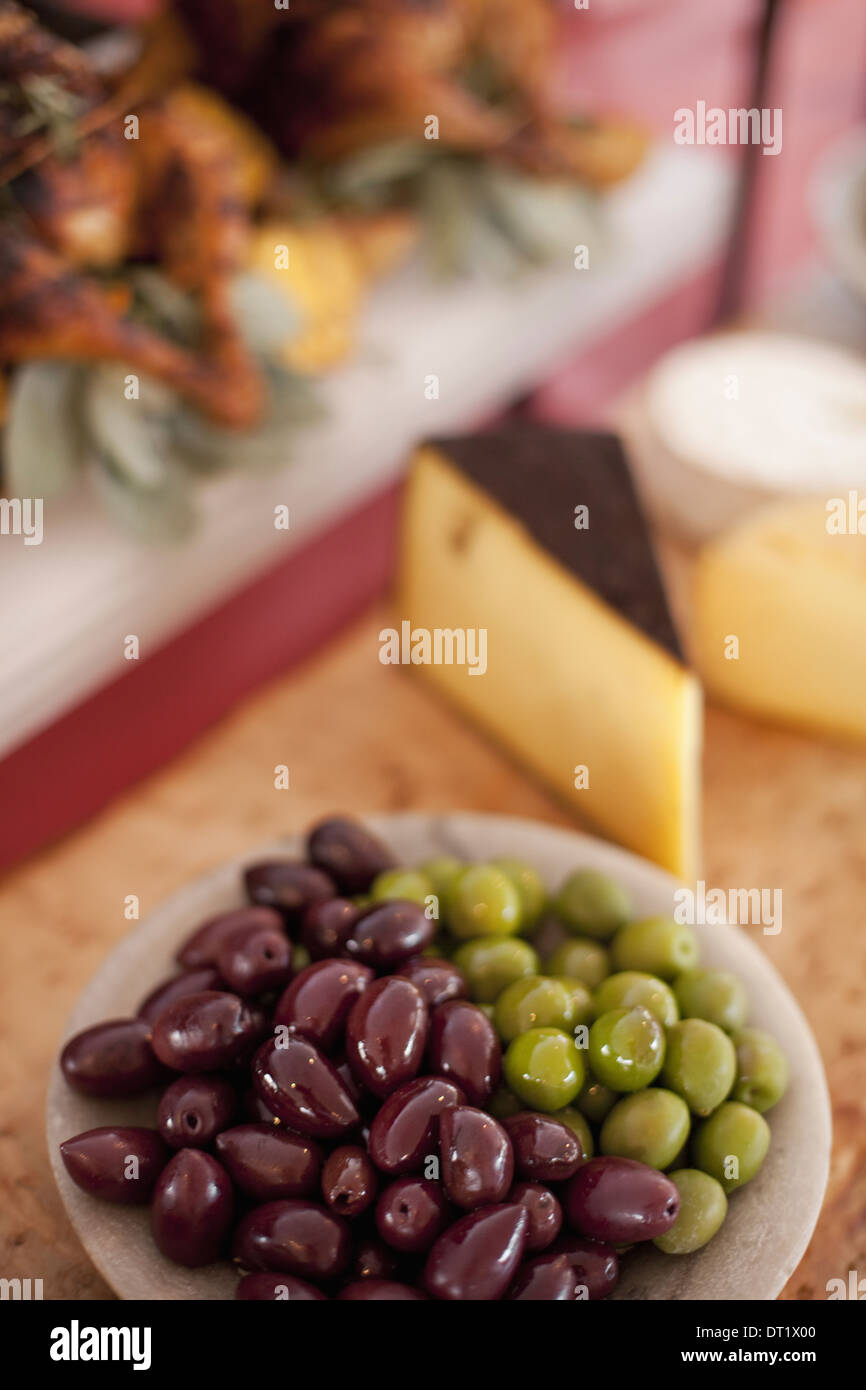 Ein Buffet-Tisch ausgelegt für eine Partei Bio-Lebensmittel A Board Käseauswahl und einen Teller mit grünen und schwarzen Oliven Stockfoto
