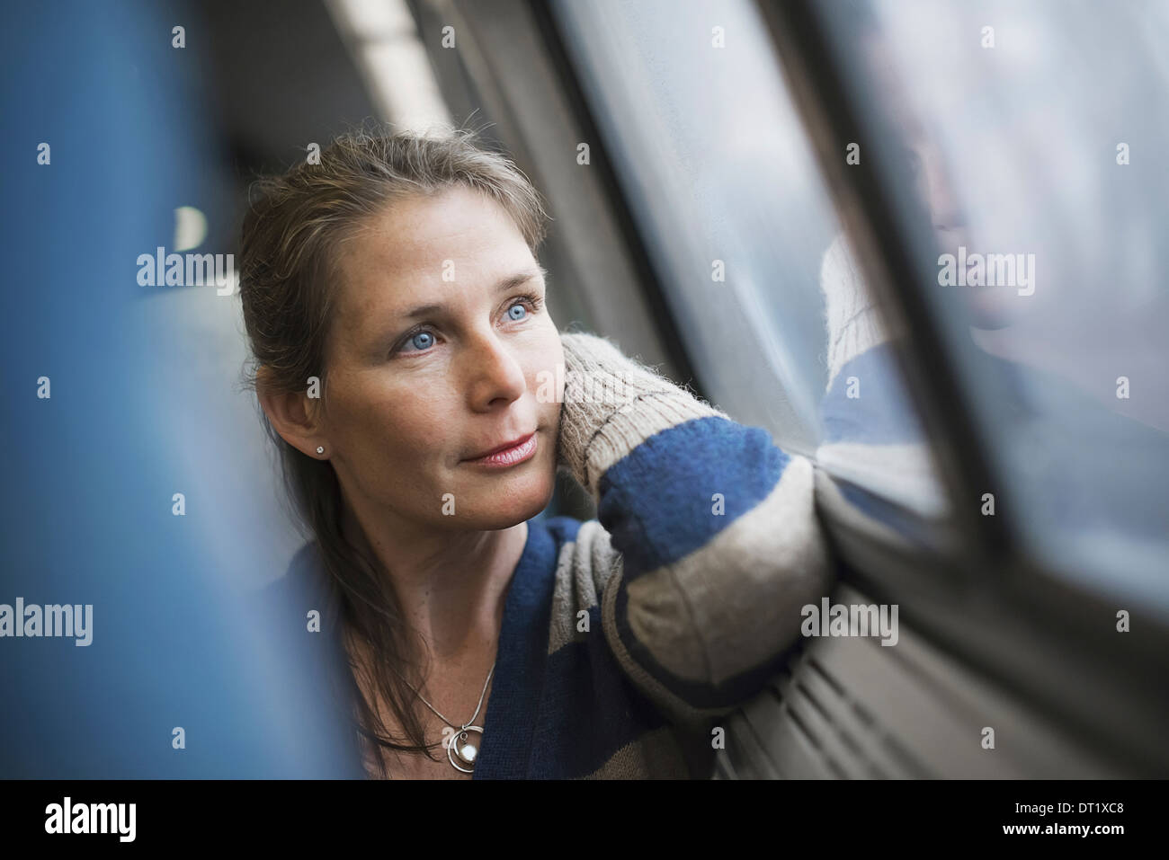 Eine Frau sitzt an einem Fensterplatz in einem Zug Wagen ihren Kopf auf ihre Hand ruht Blick in die Ferne Stockfoto