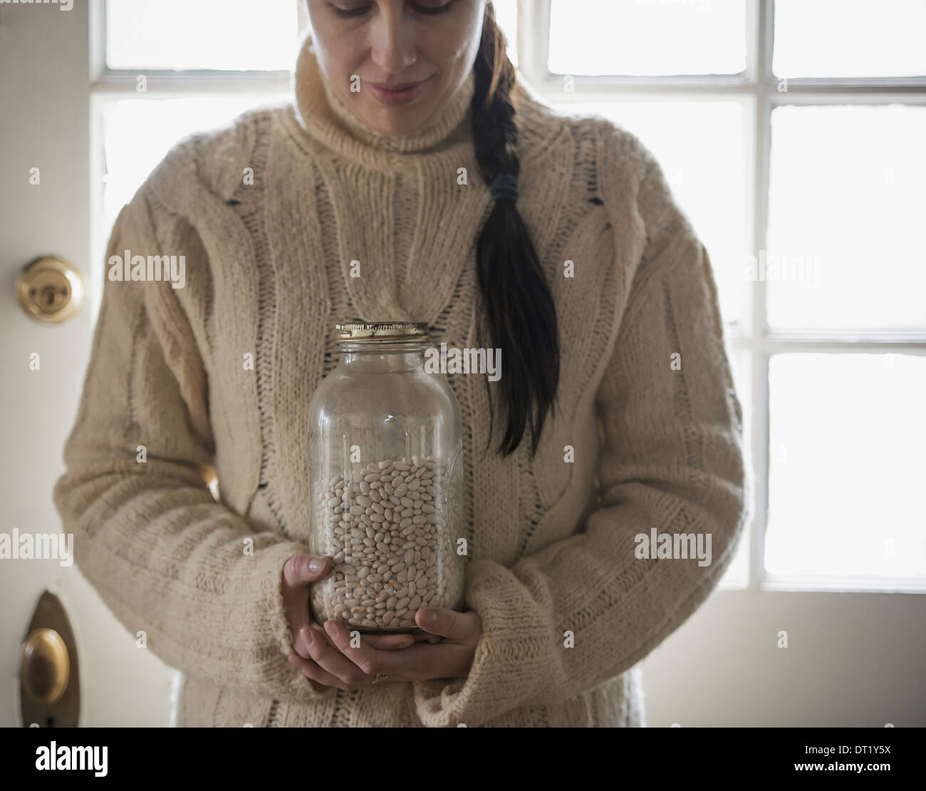 Eine Frau in einem Kabel Pullover hält ein Glas weiße Bohnen Stockfoto