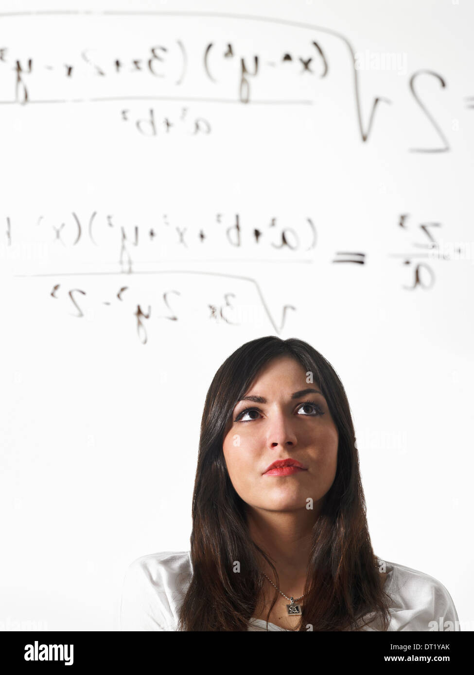 Eine junge Frau schreibt eine mathematische Gleichung mit schwarzem Filzstift auf einer klar durchsichtigen Oberfläche und stehend zurück zu betrachten Stockfoto