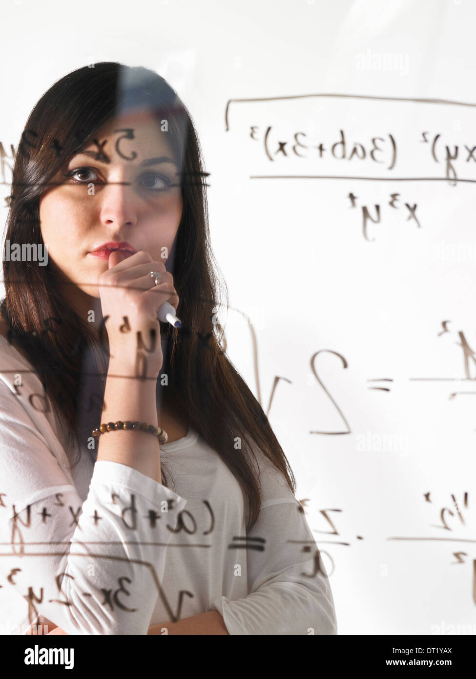 Eine junge Frau, Blick auf eine mathematische Gleichung mit schwarzem Filzstift auf einer klar durchsichtigen Wand ausgeschrieben Stockfoto