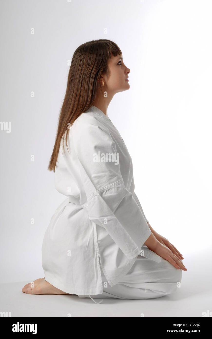 Mädchen in weißen Uniform sitzt auf Beinen in traditionellen Pose, Gesicht gestiegen Stockfoto