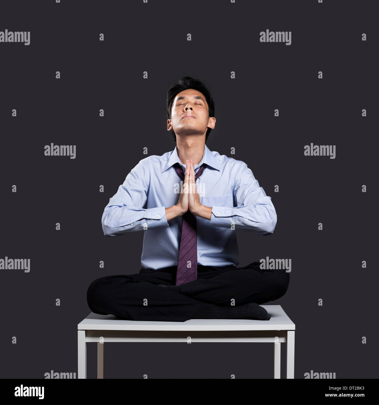 Asiatische Geschäftsmann entspannend auf Schreibtisch in Yoga Lotus-Position. Dunkel grau hinterlegt Stockfoto