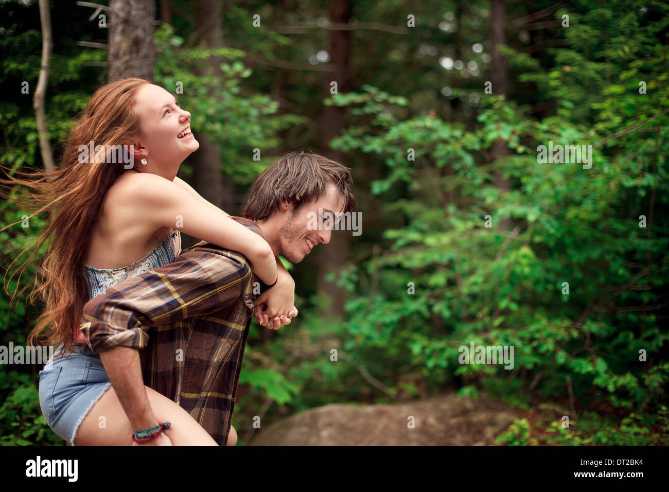 Junger Mann und junge Frau Huckepack Fahrt durch Wald Stockfoto