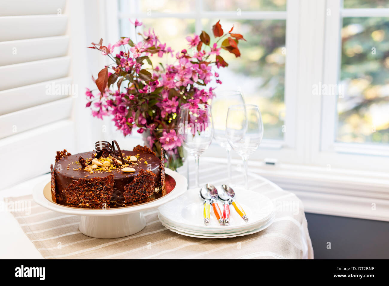 Runde Gourmet-Schokolade Kuchen auf den Tisch neben Fenster mit Tellern, Besteck und rosa Frühlingsstrauß Stockfoto