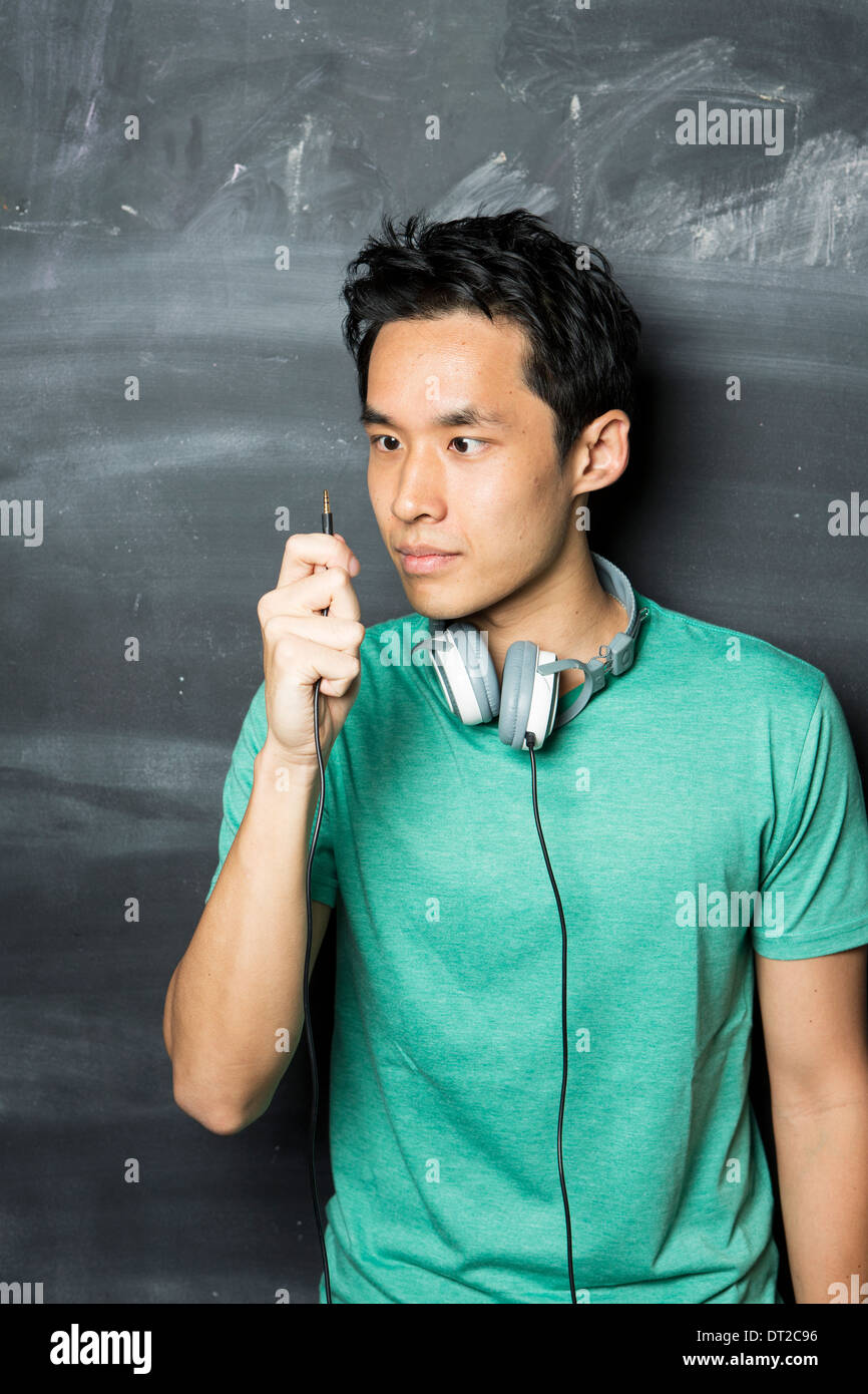 Schöner asiatischer Mann tragen Kopfhörer, singen und tanzen zur Musik. Steht man vor einer Tafel. Stockfoto
