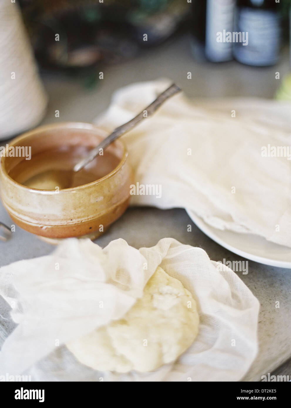 Eine Tischplatte in einer heimischen Küche A Schüssel Flüssigkeit mit einem Löffel drin eingewickelt ein Block von frischem Gebäck teilweise in einem Musselin-Quadrat Stockfoto