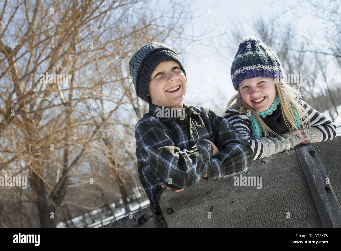 Winterlandschaft mit Schnee auf dem Boden zwei Kinder in Strickmützen stützte sich auf einen Zaun Stockfoto