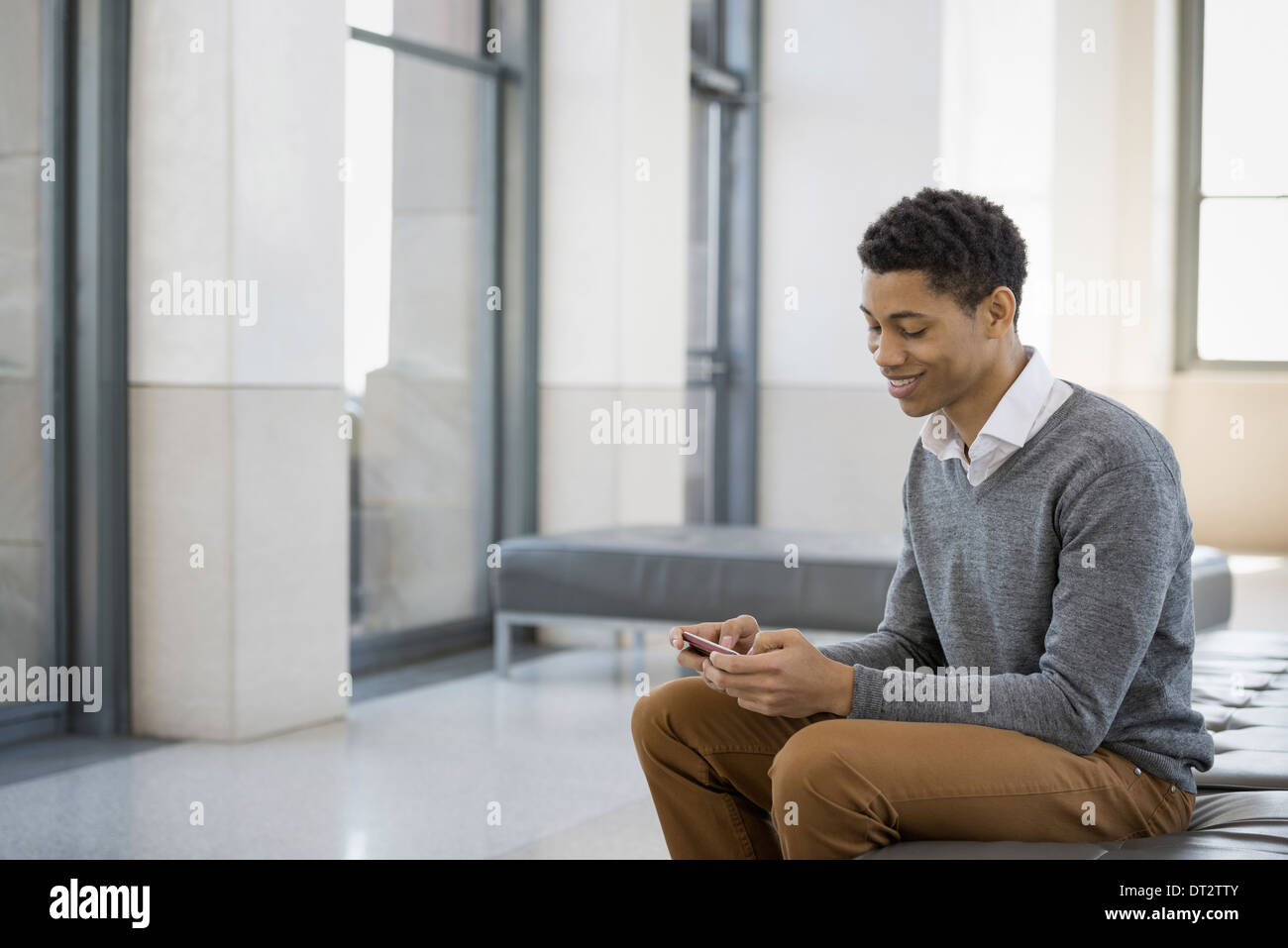 Urban Lifestyle A junger Mann sitzt in der Lobby auf eine Sitzbank mit seinem Mobiltelefon Stockfoto
