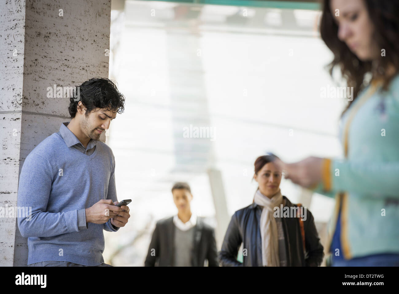 Drei Menschen auf dem Bürgersteig ein Mann und eine junge Frau mit ihren Mobiltelefonen und zwei Menschen zu Fuß auf dem Bürgersteig Stockfoto