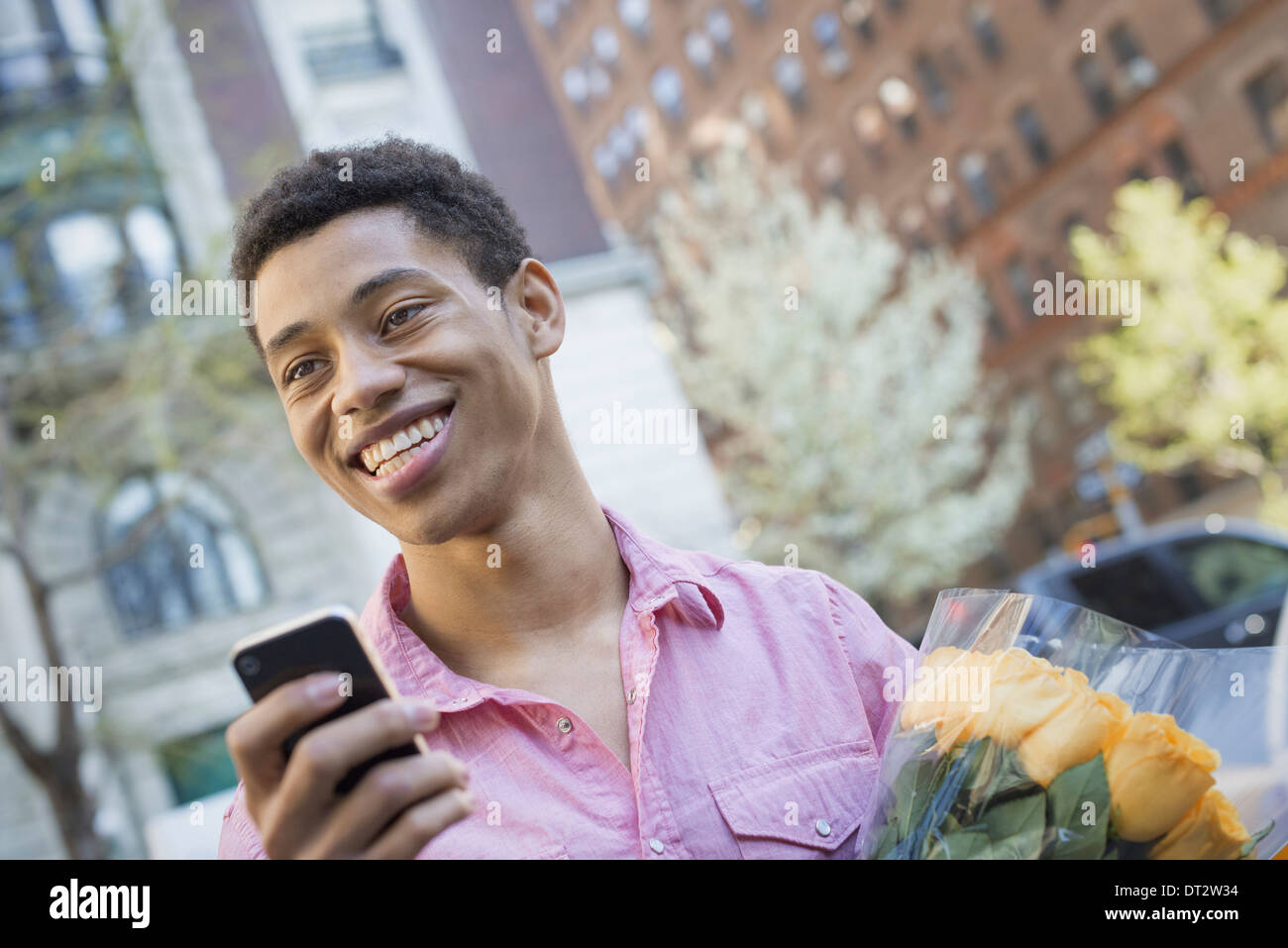 Urban Lifestyle A junger Mann mit kurzen schwarzen Haaren, trägt ein rosa casual Hemd Holding ein smart phone Stockfoto