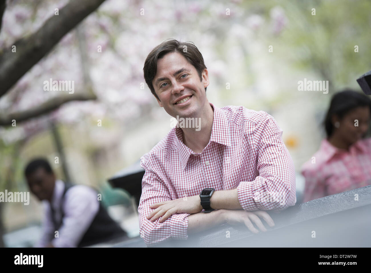 Blick über CityA Mann sitzt im Freien in einer Stadt parken Looking in die Kamera und lächelnd Stockfoto