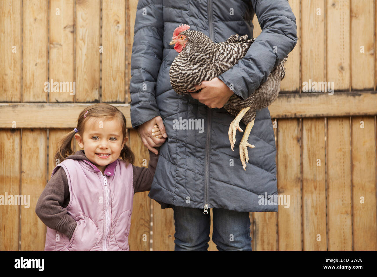 Eine Frau hält ein schwarzen und weißes Huhn mit einem roten Coxcomb unter einem Arm ein junges Mädchen neben ihr Betrieb ihrer anderen Seite Stockfoto