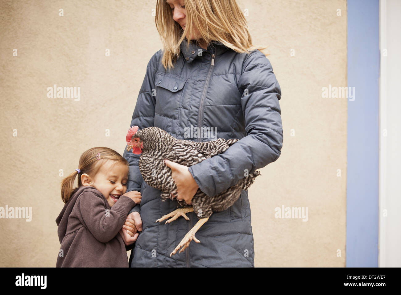 Eine Frau hält ein schwarzen und weißes Huhn mit einem roten Coxcomb unter einem Arm ein junges Mädchen neben ihr Betrieb ihrer anderen Seite Stockfoto