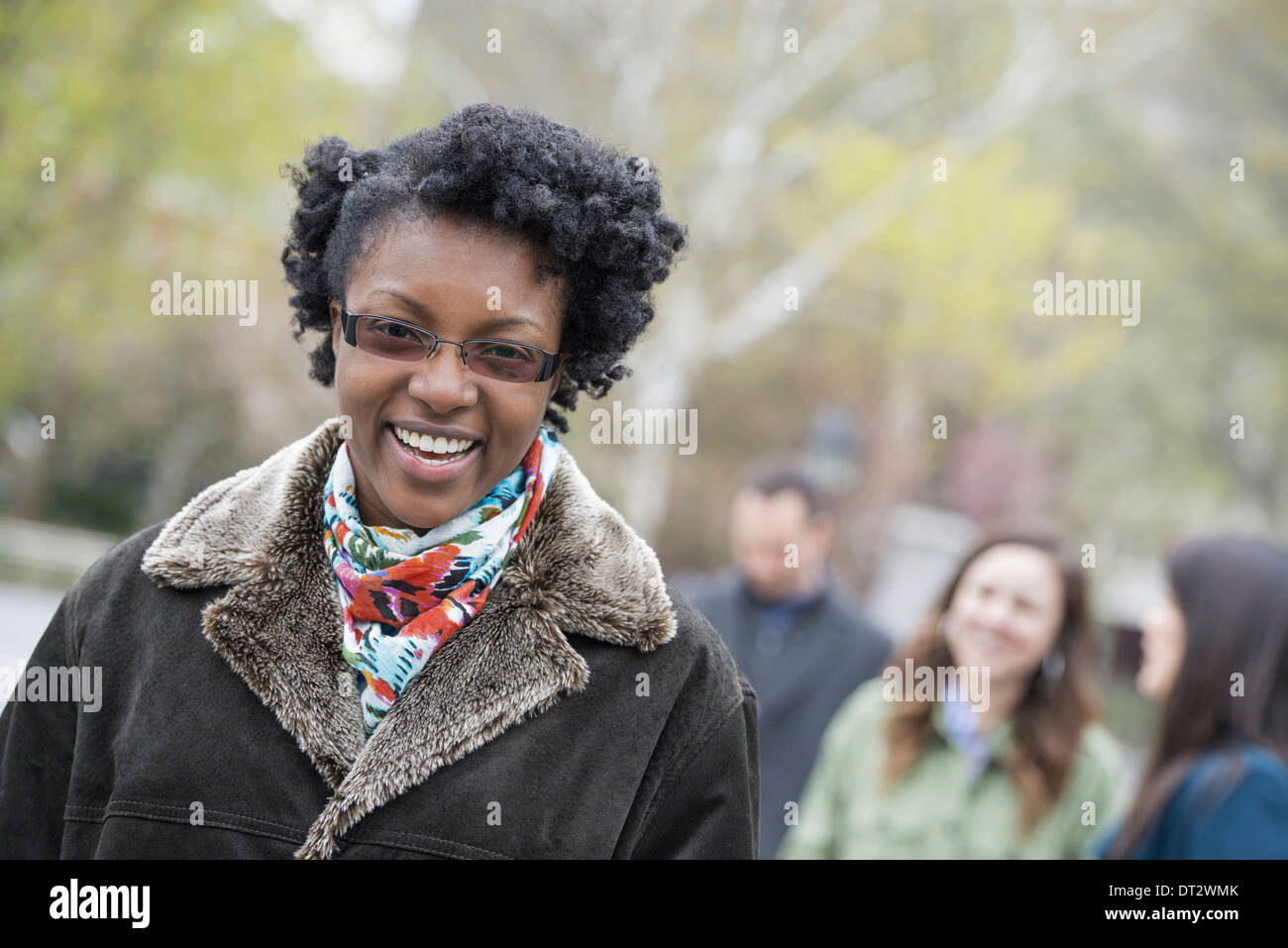 Eine Gruppe von Menschen in einer Stadt parken eine junge Frau in einem Mantel mit einem großen Kragen lächelt und schaut in die Kamera Stockfoto