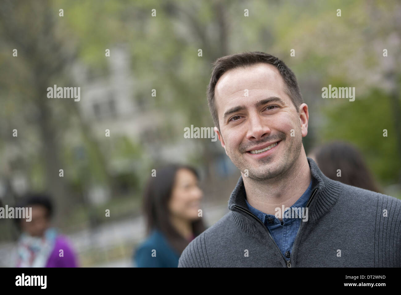 Eine Gruppe von Menschen in einer Stadt parken einen lächelnder Mann in einem grauen Pullover Stockfoto