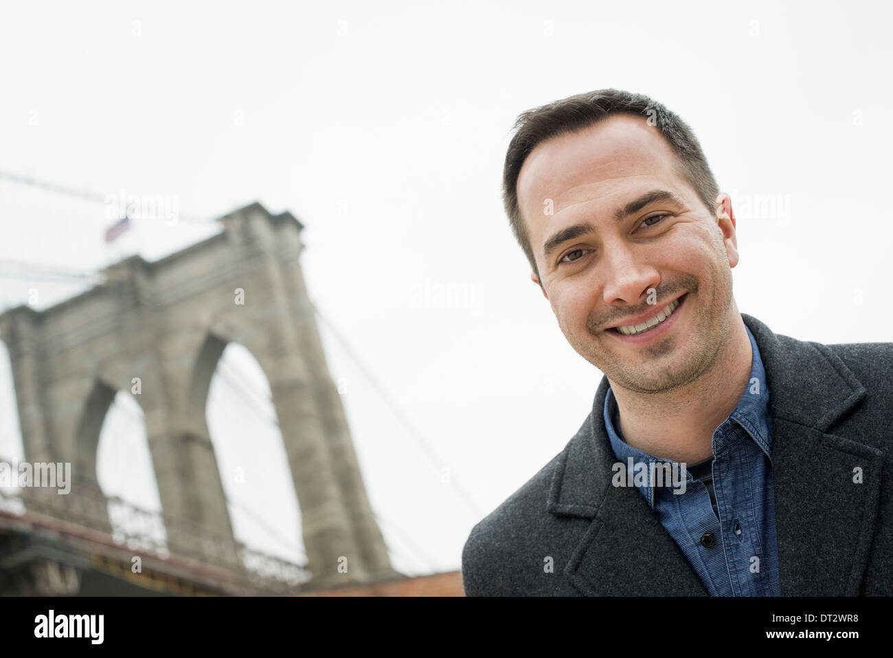 New Yorker Brooklyn Bridge überqueren den East River A Mann schaut in die Kamera und lächelnd Stockfoto