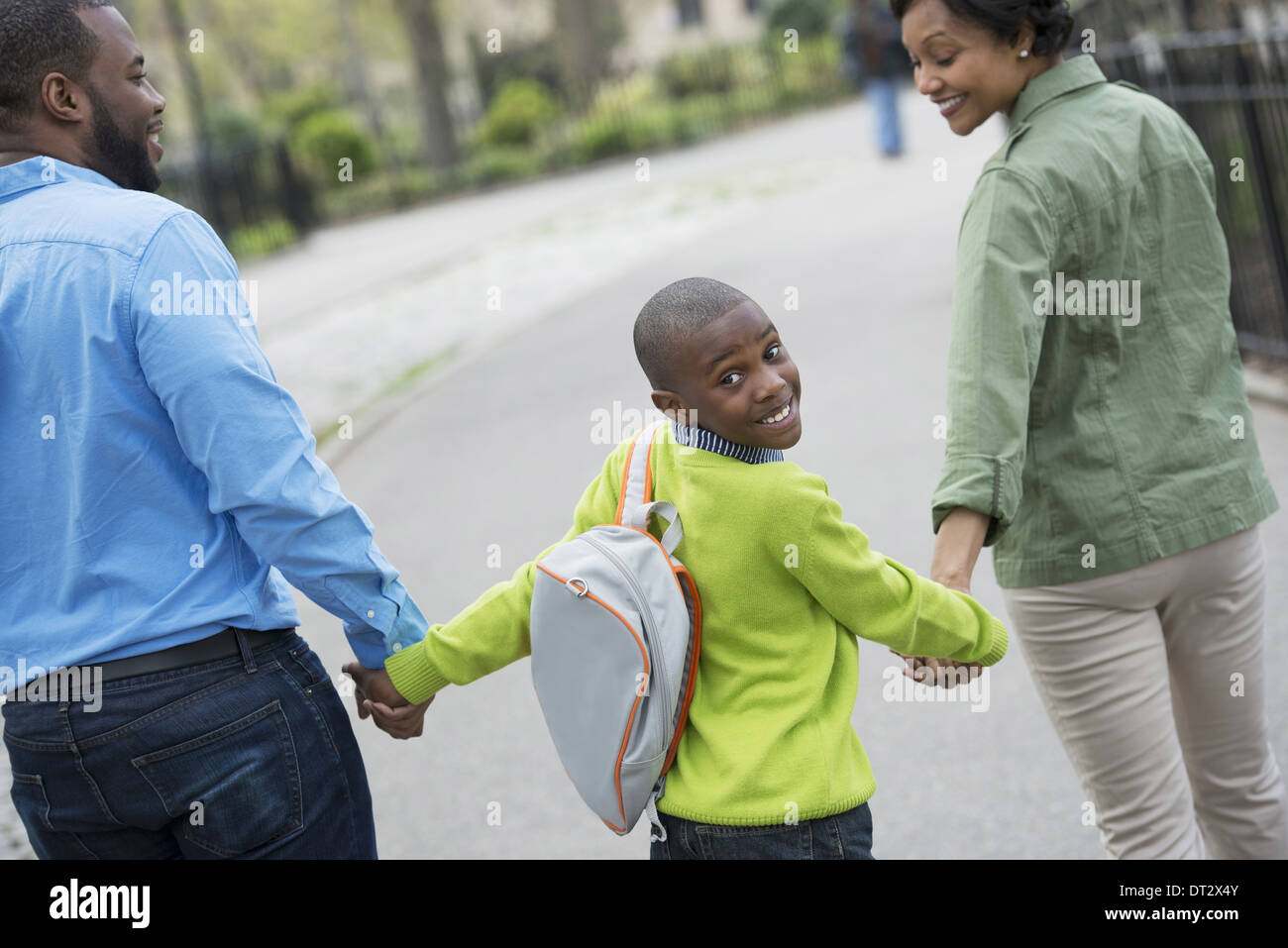 Ein Junge mit einer Schultasche, Hand in Hand mit seiner Mutter und Vater Stockfoto
