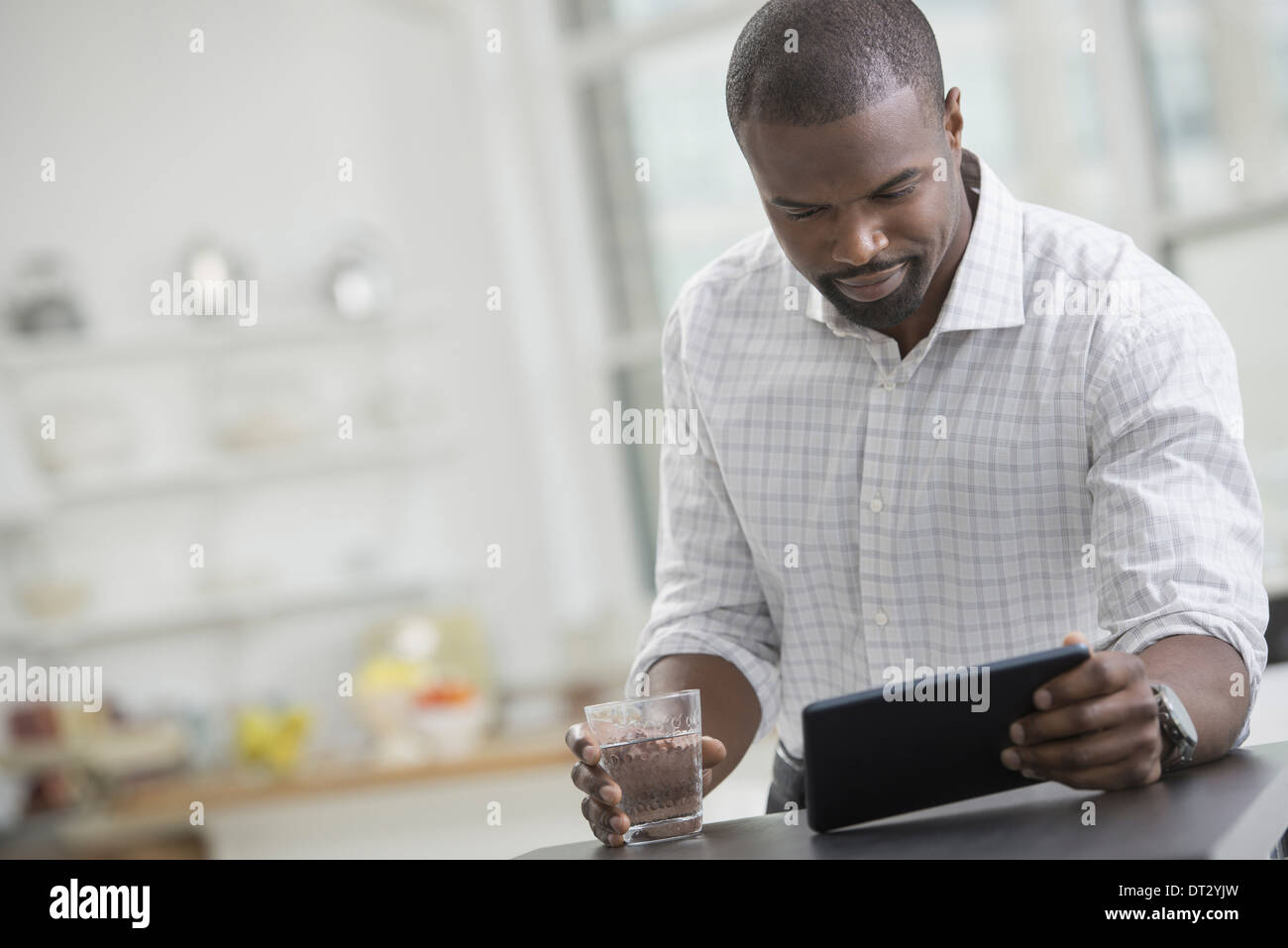 Junge Berufstätige Arbeit A Geschäftsmann in einem offenem Kragen sitzen mit einem Glas Wasser mit einem digitalen tablet Stockfoto