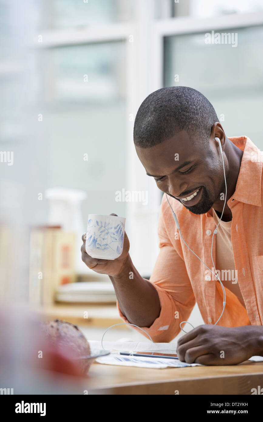 Ein Mann in einem orangefarbenen t-Shirt beim Frühstück mit einer Tasse Tee Stockfoto