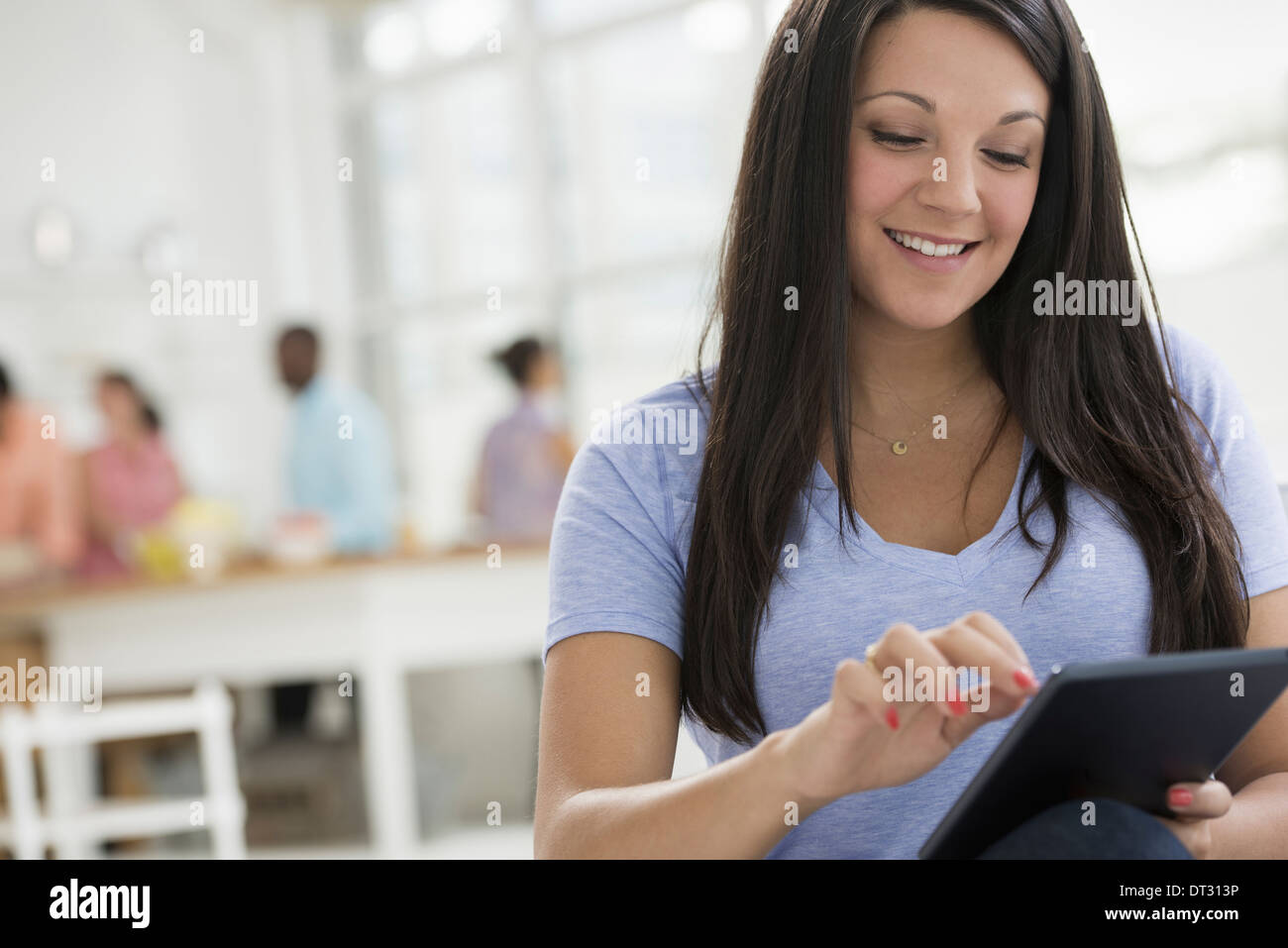 Eine Frau mit langen schwarzen Haaren, die mit einem digitalen Tablet Menschen im Hintergrund Stockfoto