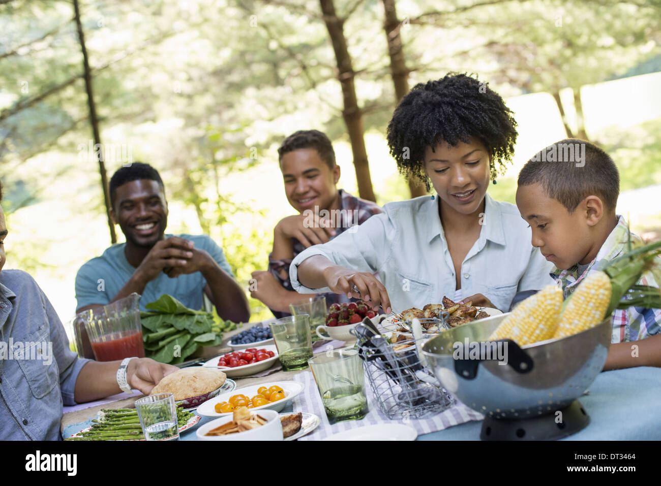 Ein Familien-Picknick in einem schattigen Waldgebiet Erwachsene und Kinder an einem Tisch reichte um Platten und Essen Stockfoto