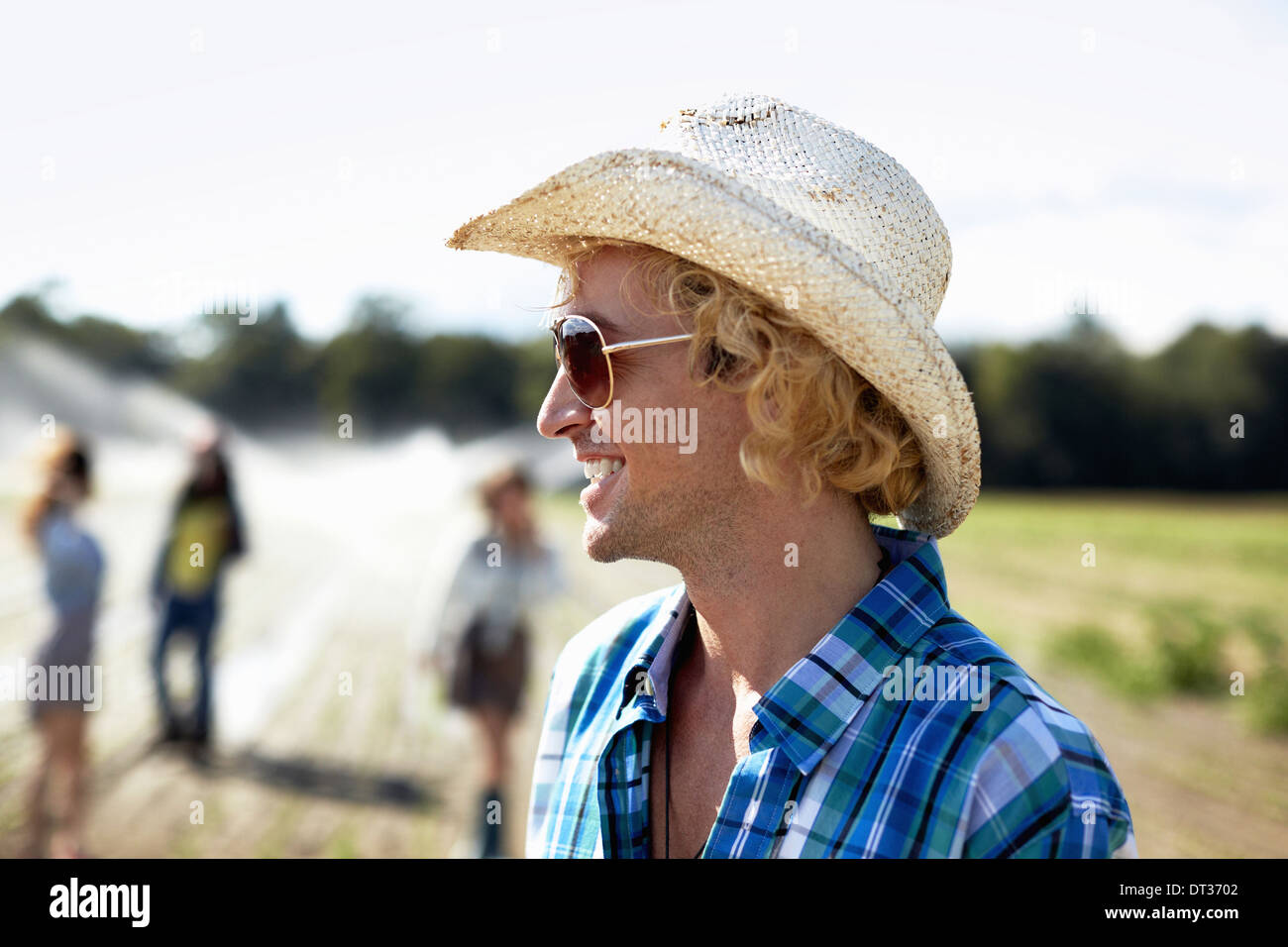 Ein junger Mann in Stroh Hut und eine Sonnenbrille Bewässerung Sprinkler im Feld Stockfoto